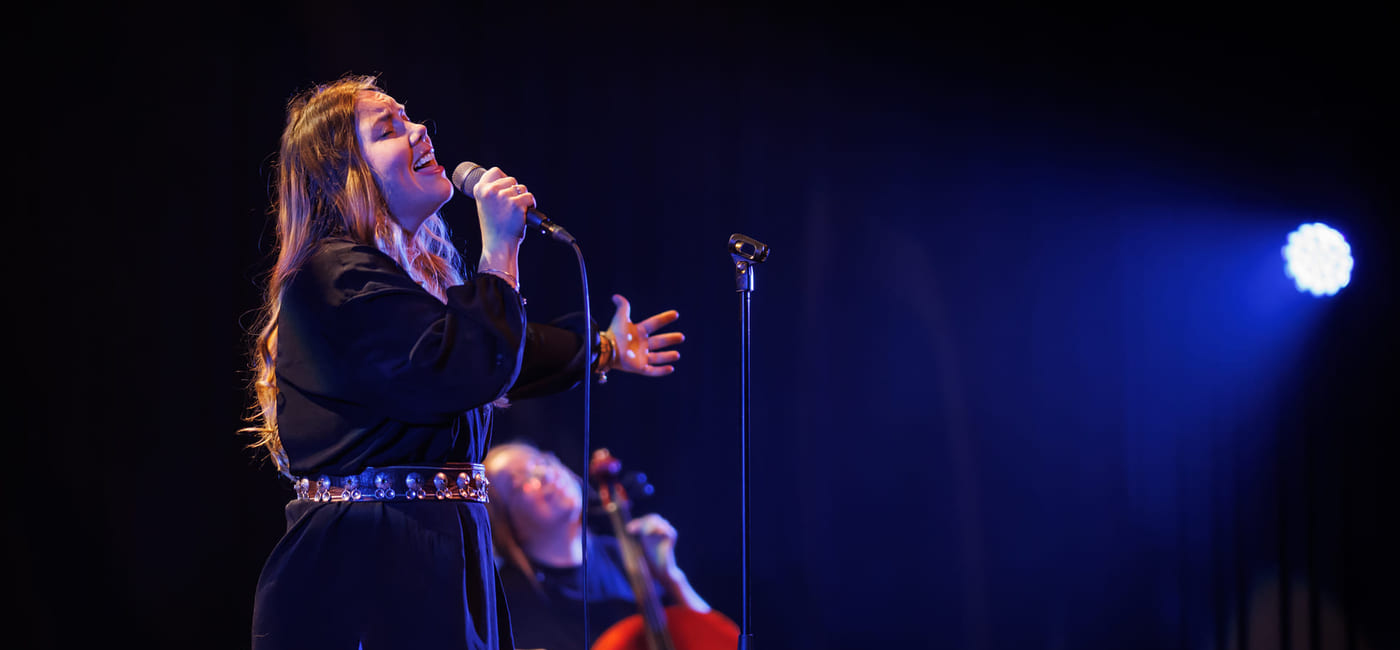 En cellist og en sanger opptrer sammen på en mørk scene med blått scenelys.