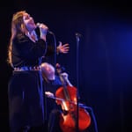 En cellist og en sanger opptrer sammen på en mørk scene med blått scenelys.