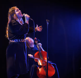 En cellist og en sanger opptrer sammen på en mørk scene med blått scenelys.