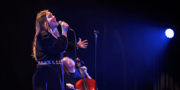 En cellist og en sanger opptrer sammen på en mørk scene med blått scenelys.