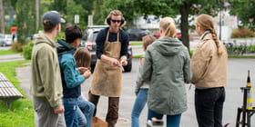 En gruppe ungdommer er samlet rundt en smed i en skolegård. Smeden har på seg verneutstyr,