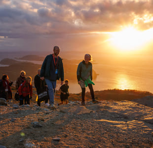 En gruppe mennesker går på et fjell i solnedgangen.