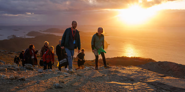 En gruppe mennesker går på et fjell i solnedgangen.