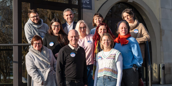 En gruppe med kvinner og men står på en trapp foran en bygning