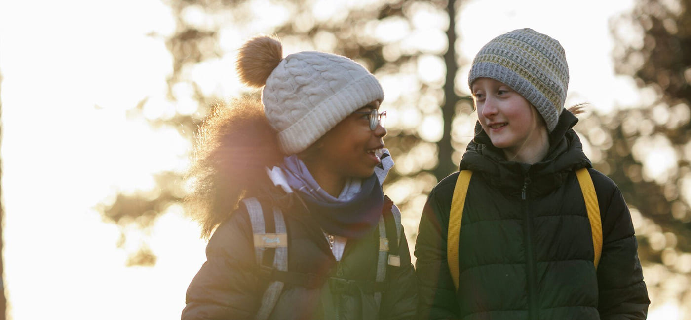 To jenter er ute og går. De smiler og ser på hverandre.