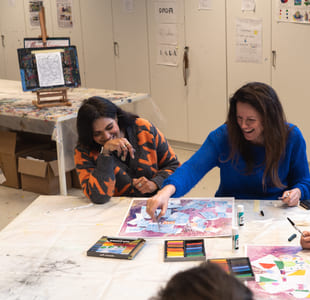 Fire mennesker sitter rundt et bord og fargelegger noe. To av damene ler.