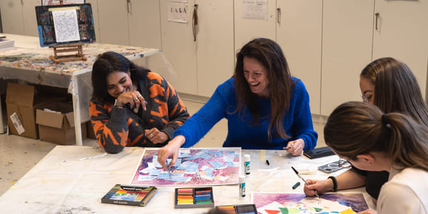 Fire mennesker sitter rundt et bord og fargelegger noe. To av damene ler.