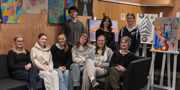 En gruppe ungdommer sitter i en halvsirkel, med fargerik kunst på veggene bak.