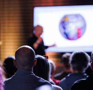 Publikum ser på presentasjon med vitenskapelig bilde på skjermen. En mann står foran skjermen.