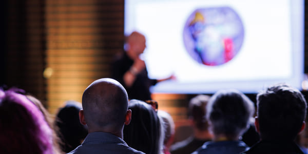 Publikum ser på presentasjon med vitenskapelig bilde på skjermen. En mann står foran skjermen.