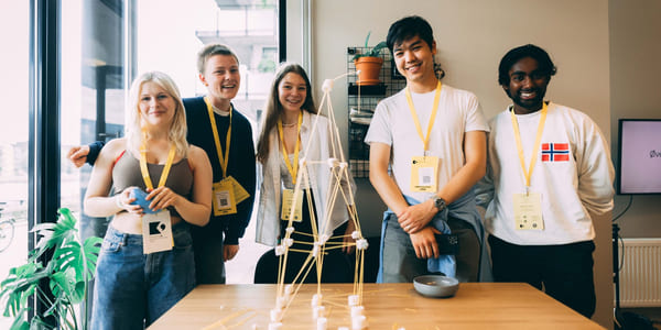 Fem ungdommer står ved et bord. De ser i kamera, i et lyst og uformelt miljø.