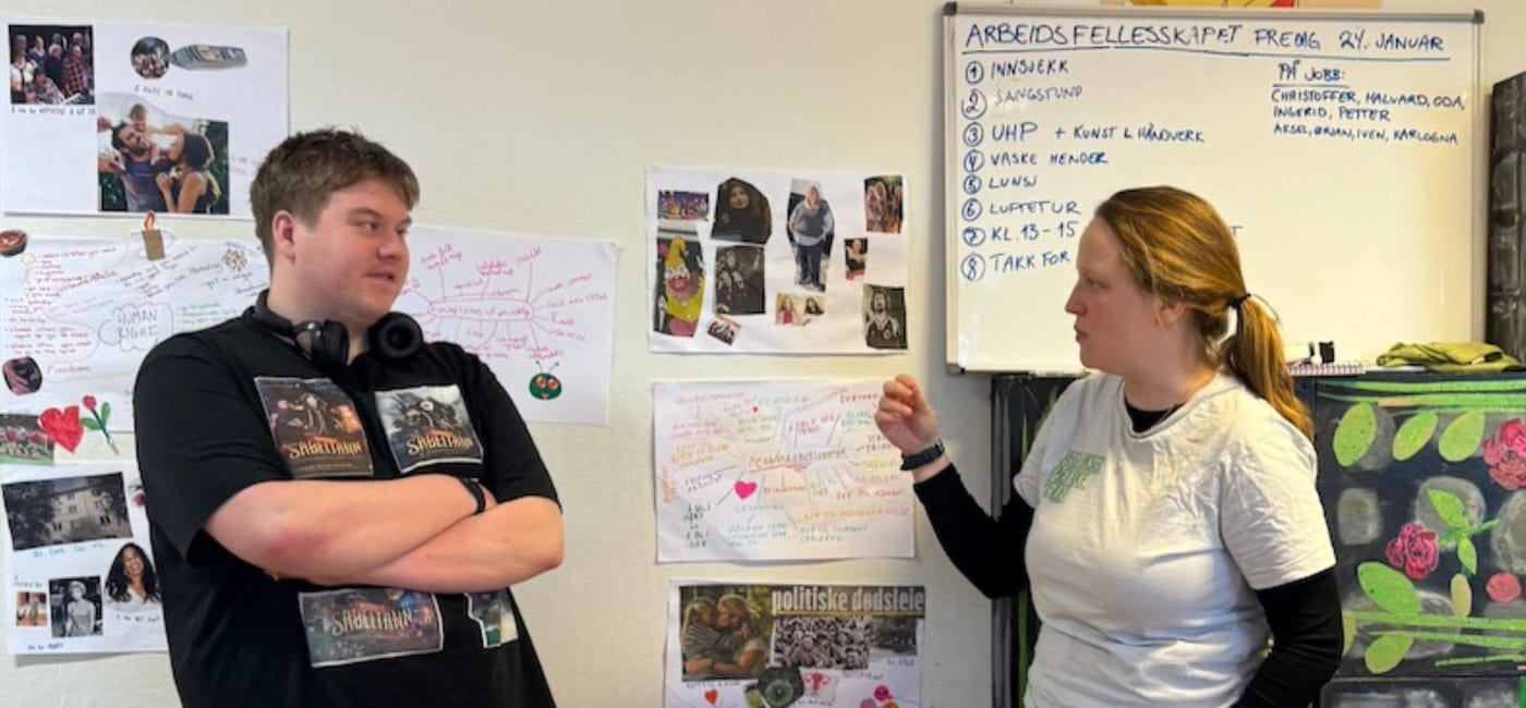 To personer står foran en plansjeutstilling og snakker sammen