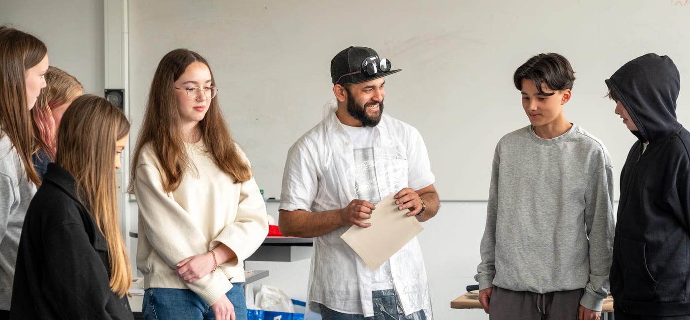Flere ungdommer står rundt et bord og samtaler, med undervisningsmateriell foran seg.