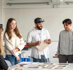 Flere ungdommer står rundt et bord og samtaler, med undervisningsmateriell foran seg.