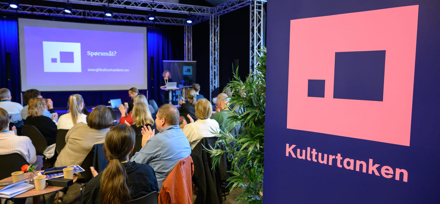 Sittende publikum ser på en presentasjon. Kulturtanken-logo på rollup i forgrunnen.