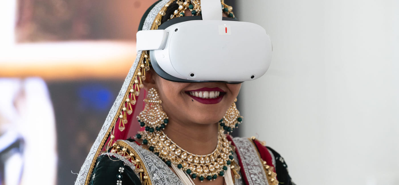Kvinne i tradisjonell indisk brudeantrekk iført et virtual reality-headset, smiler med knallrød leppestift.
