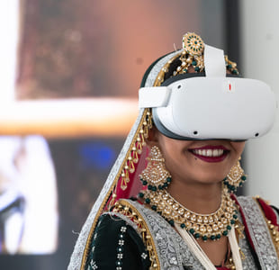 Kvinne i tradisjonell indisk brudeantrekk iført et virtual reality-headset, smiler med knallrød leppestift.