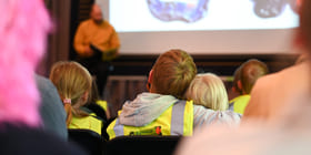 Barn i sikkerhetsvester ser på litteraturformidling. Forfatter i oransje skjorte står i nærheten av projiserte bilder av tegninger.
