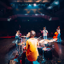 Et band bestående av ungdommer spiller musikk på en scene med fargerike scenelys.
