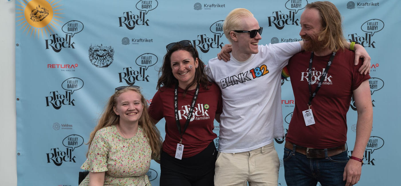 Fire personer smiler foran fotovegg med festivalens logo.