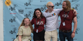 Fire personer smiler foran fotovegg med festivalens logo.