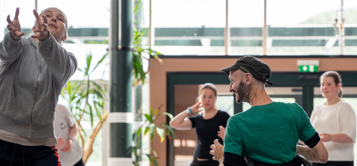 Mennesker danser sammen i et stort, opplyst rom. En av dem sitter i rullestol.