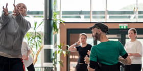 Mennesker danser sammen i et stort, opplyst rom. En av dem sitter i rullestol.