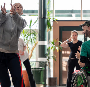 Mennesker danser sammen i et stort, opplyst rom. En av dem sitter i rullestol.