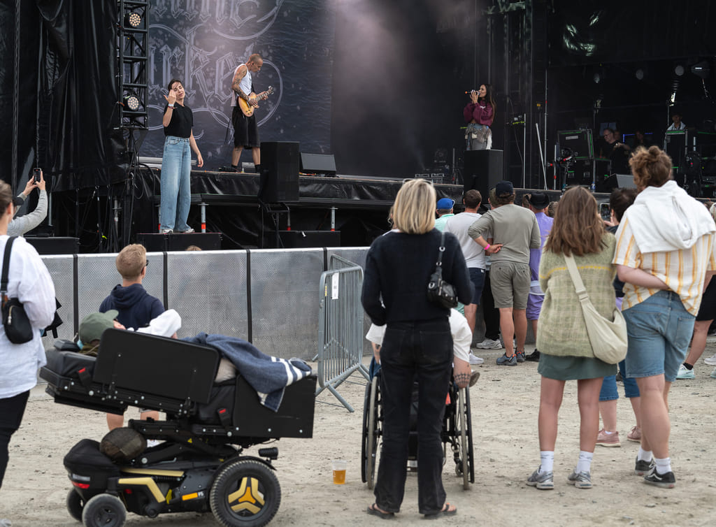 Publikum ser på sceneopptreden – flere rullestolbrukere i forgrunnen.