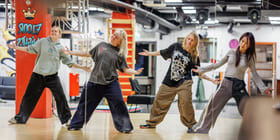 Fire jenter danser i et dansestudio. De har på seg avslappede klær.