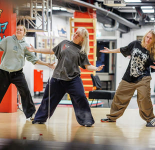 Fire jenter danser i et dansestudio. De har på seg avslappede klær.