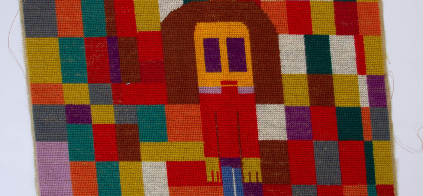 Et fargerikt vevd teppe. I midten ses en menneskefigur.