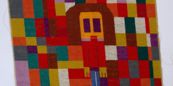 Et fargerikt vevd teppe. I midten ses en menneskefigur.