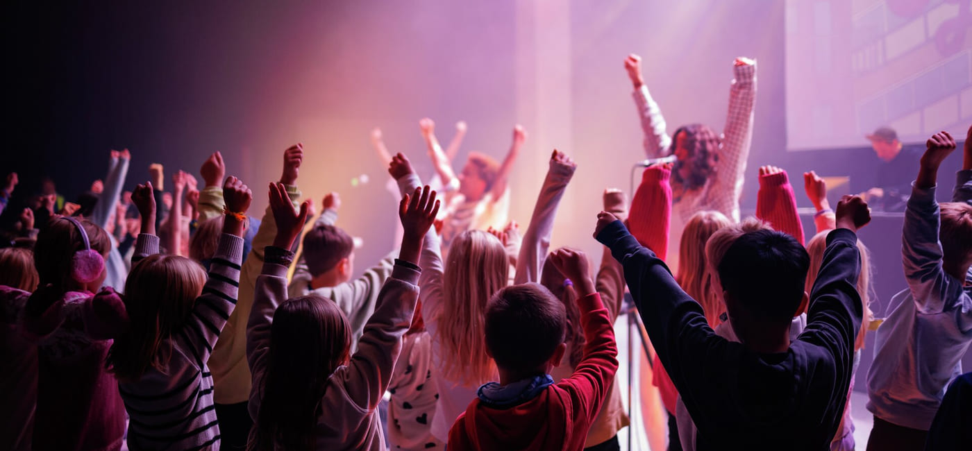 Folkemengde med hevede armer på en konsert, badet i levende lilla og rød belysning.