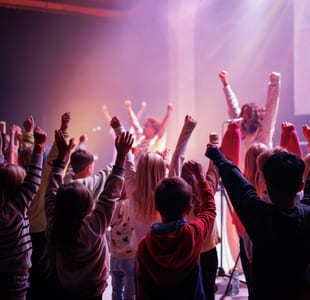 Folkemengde med hevede armer på en konsert, badet i levende lilla og rød belysning.