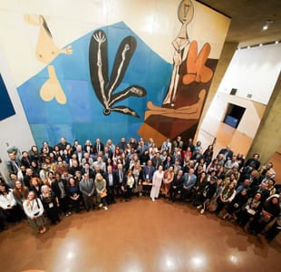 Stort gruppebilde av ulike deltakere på en internasjonal konferanse, med fargerikt abstrakt veggmaleri og flerspråklig skilt i bakgrunnen.