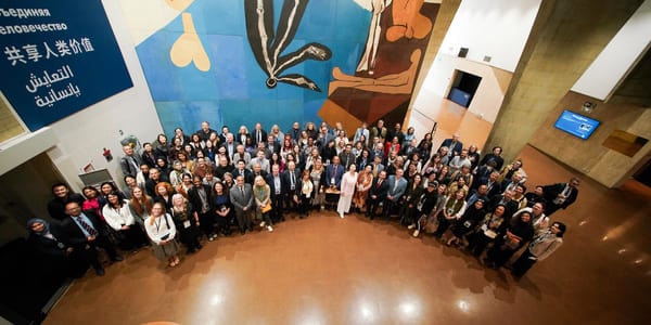 Stort gruppebilde av ulike deltakere på en internasjonal konferanse, med fargerikt abstrakt veggmaleri og flerspråklig skilt i bakgrunnen.