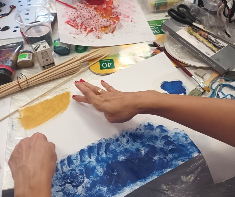 Hender lager kunst med maling og pensel på papir, omgitt av kunstutstyr.