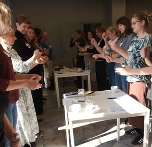 Gruppe deltar i en aktivitet rundt bord med materialer i et innendørs rom.