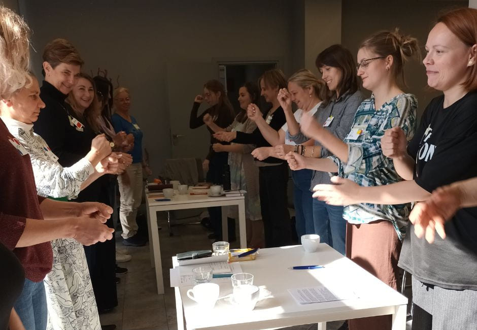 Gruppe deltar i en aktivitet rundt bord med materialer i et innendørs rom.