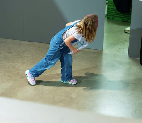 En jente i dongeridress utforsker innendørsrommet på betonggulv.