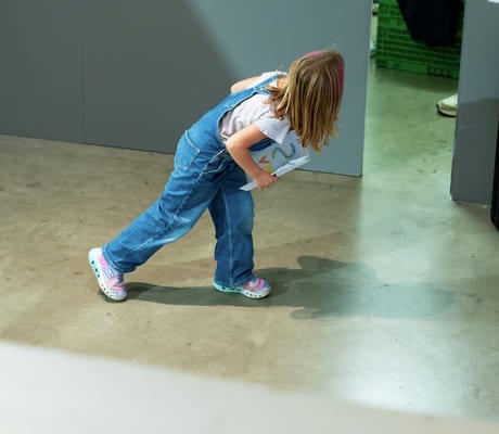 En jente i dongeridress utforsker innendørsrommet på betonggulv.