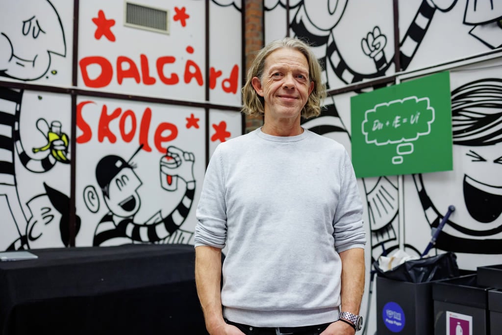 Person i hvit genser står foran et fargerikt veggmaleri med tekst og tegneserieaktige tegninger fra Dalgard skole.