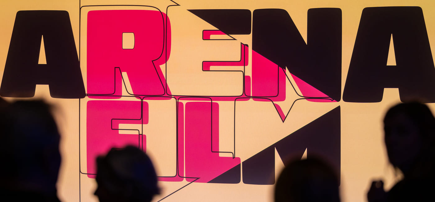 Silhuetter av fire mennesker som står foran en kinoskjerm som viser logoen til Arena Film.