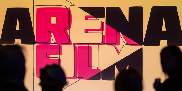 Silhuetter av fire mennesker som står foran en kinoskjerm som viser logoen til Arena Film.