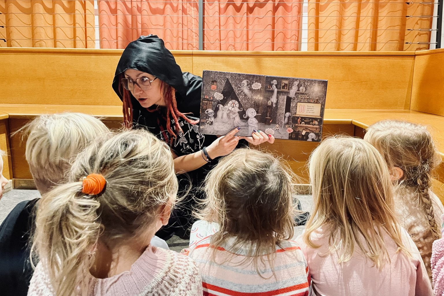 En kvinne med hette over hodet viser fram en bildebok til en gruppe barn.