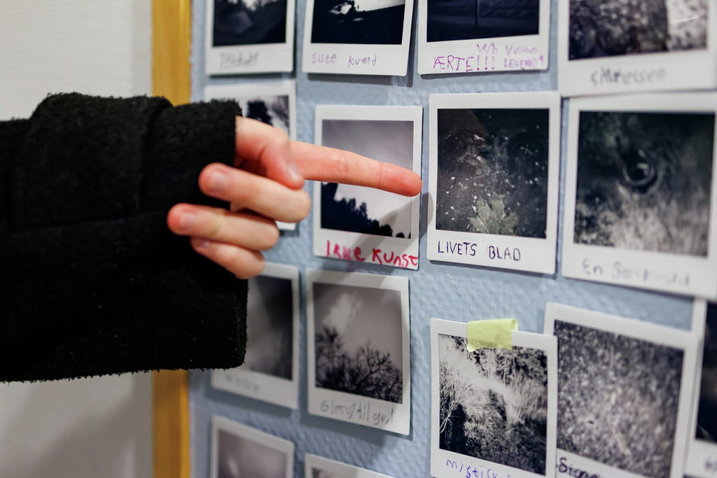 Håndvalg av bilde fra en vegg med små polaroidbilder vist i et organisert rutenett.