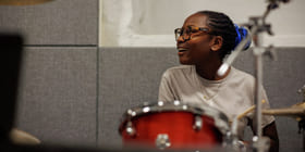 Ei jente med briller spiller trommer