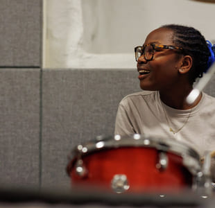 Ei jente med briller spiller trommer