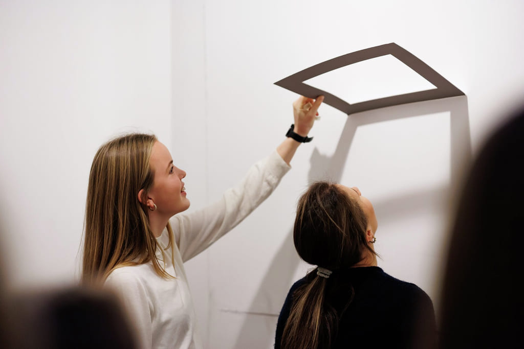 Kvinne installerer eller justerer en firkantet lysarmatur i taket mens hun står på en stige.